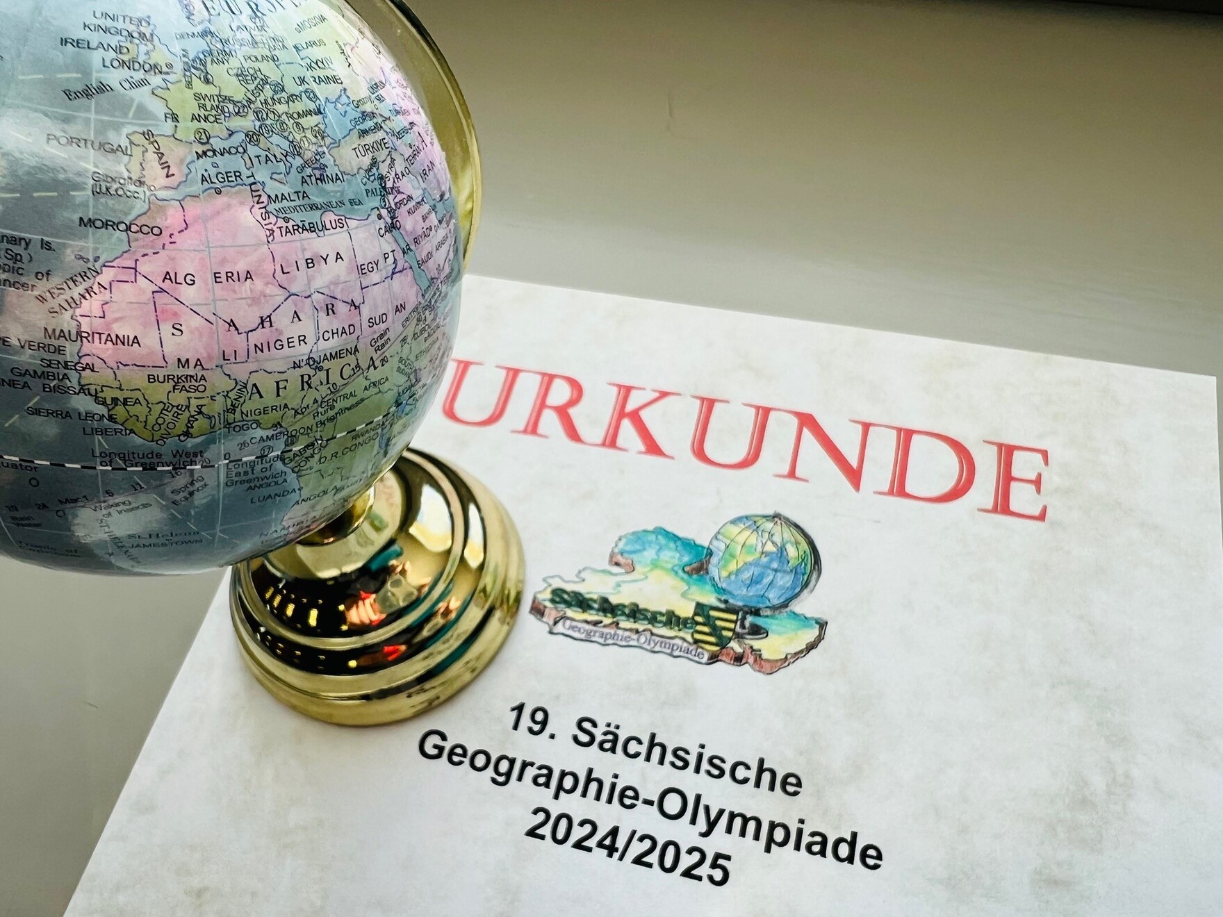 Urkunde des 19. Regionalfinales der Geographieolympiade und ein Globus