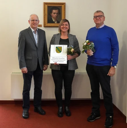Das Bild zeigt die Ehrung von Susanne Schmitt zum Öffentlich bestellten Vermessungsingenieur. Außerdem sind zwei weitere Herren mit auf dem Bild.