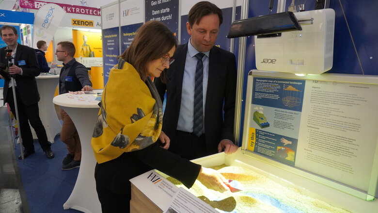 Ronny Zienert und Barbara Meyer testen etwas mit Sand und einer kleinen Schaufel aus.
